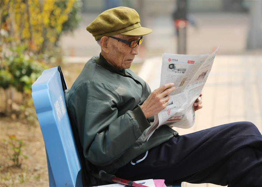 周智夫在干休所小花园中阅读报纸(2015年4月9日摄)。